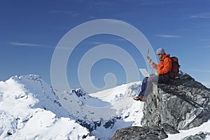 Mountain Climber Using Laptop And Walkie Talkie On Mountain Peak