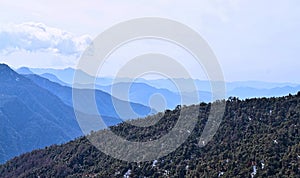 Mountain Covered by Dense Forest and Ranges of Blue Himalayan Mountains at Distance in Background with Sky - Aerial Landscape
