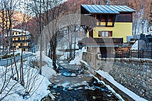 Mountain creek flows along a snowy shore and a wooden house.