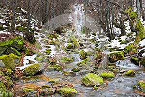 Mountain creek, snow and moss covered rocks and iconic waterfall Tupavica