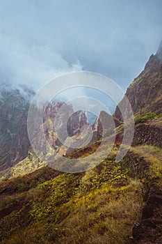 Mountain edge overgrown with verdant grass along the trekking path. Mountain peaks are encase by fog . Xo-Xo Valley