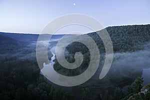 Mountain forest landscape. Trees and the river in the fog in the early morning.