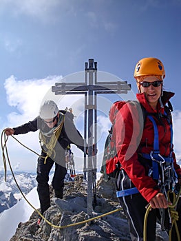 Mountain guide and woman client arrive at the summit cross of a high alpine peak in the Swiss Alps