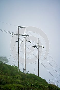 Mountain with high voltage electricity. Transmission tower in meadow and smooth fog. Electrical Power Line and Pylon with Misty