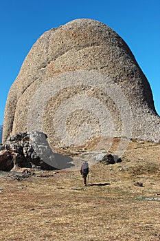 Mountain hiker with backpack approaches giant stone rock