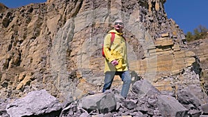 Mountain hiker. Man run in the mountains in a yellow raincoat and a red backpack. Guy looking around. Sport orienteering