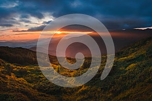 Mountain hill with stormy sky and sunbeam at sunset