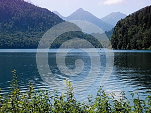 Mountain lake Alpsee with turquoise colored clean deep water. Smoky purple mountains on horizon