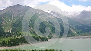 Mountain lake `Big Almaty Lake`.  View of green hills, mountains, grass and flowers.