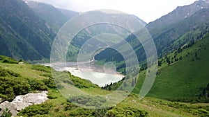 Mountain lake `Big Almaty Lake`.  View of green hills, mountains, grass and flowers.