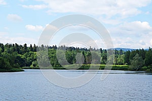 Mountain lake with cold dark water surrounded by green forest under a blue sky