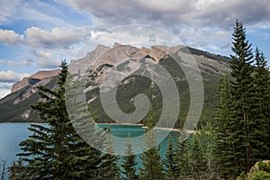 Mountain lake - coniferous forest - pine trees, scenic blue lake, cloudy sky and Rocky Mountains on horizon background.