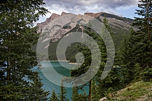 Mountain lake - coniferous forest - pine trees, scenic blue lake, cloudy sky and Rocky Mountains on horizon background.