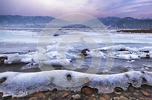 Mountain lake covered with ice, snow and hummocks in early spring at sunset. Bartogay reservoir in Kazakhstan with frozen waves