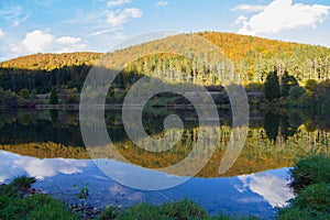 a mountain with a lake in front of it and trees in the background with a blue sky and clouds