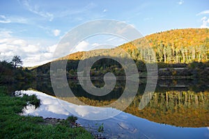 a mountain with a lake in front of it and trees in the background with a blue sky and clouds