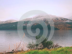 Mountain lake before misty sunset in Higland in Scotland. Snowy cone of mountain above mirroring water photo