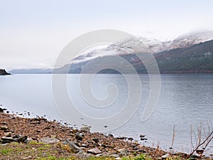 Mountain lake before misty sunset in Higland in Scotland. Snowy cone of mountain above mirroring water