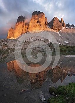 Mountain lake reflecting the mountains of the Three Peaks in the European Dolomite Alps with alpenglow during sunset, South Tyrol
