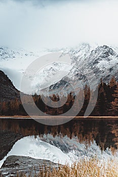 Mountain lake with reflection in the mirrored surface of the rocks in cloudy rainy weather.