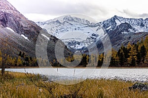 Mountain lake with reflection in the mirrored surface of the rocks in cloudy rainy weather.