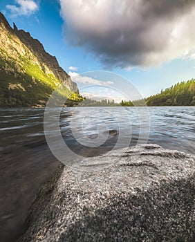 Horské jezero se skálou v popředí a částečně osvětleným kopcem