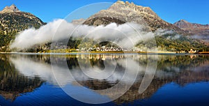 Mountain lake at sunrise in autumn. Landscape with lake, gold sunlight, blue fog over the water, reflection, trees with colorful