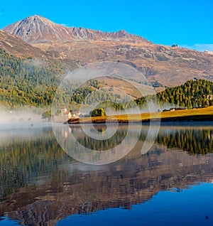 Mountain lake at sunrise in autumn. Landscape with lake, gold sunlight, blue fog over the water, reflection, trees with colorful