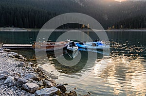 Mountain lake sunrise landscape.Old wooden boat and blue kayaks at the plank