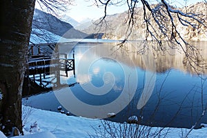 Mountain lake in winter. Pier house and tree branches covered with snow. Snowy mountains
