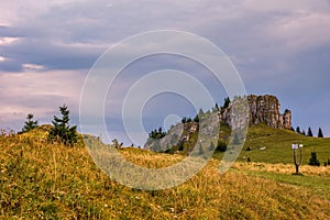 Horská krajina s krásnou farebnou oblohou, skalnatým bralom a horskými lúkami so stromami.