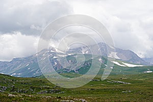 Mountain landscape with clouds and green alpine meadows in the foreground.