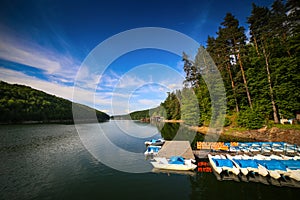 Mountain landscape with docks and pedal cycle boats on lake Gozna surrounded by forest at Valiug