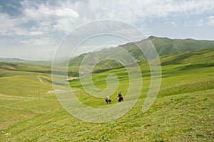 Mountain landscape with green grass valley and riders on horseback