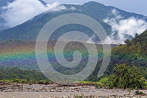 Mountain landscape with a rainbow over river.