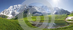 Mountain landscape of Svaneti on bright summer sunny day. Mountain lake, hills covered green grass on snowy rocky mountains