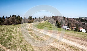 Horská lúka s turistickým chodníkom, pár domov, les a jasná obloha na Slovensku