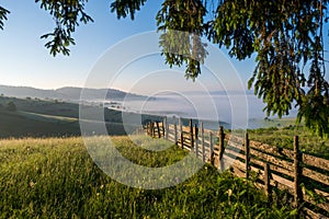 Mountain meadow in a sunrise enclosed by a wooden fence