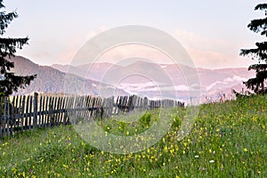 Mountain meadow with a wooden fence, view on the mountains, early morning