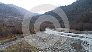 Mountain narrow river and stony shore along high forested mountains. Shot. Aerial autumn landscape, orange hill slopes