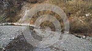 Mountain narrow river and stony shore along high forested mountains. Shot. Aerial autumn landscape, orange hill slopes