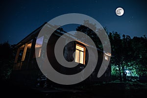 Mountain night landscape of building at forest at night with moon or vintage country house at night with clouds and stars. Summer