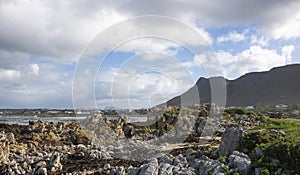 Mountain and ocean sunset view with vacation homes in the background and rocks in the foreground.