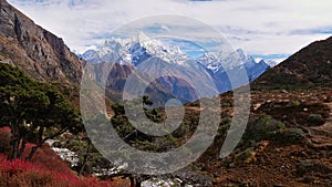 Mountain panorama in the Himalayas including Thamserku with red colored bushes and coniferous trees on foreground.