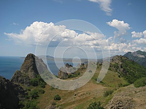 Mountain panorama of picturesque peaks covered with fresh green grass against the background of a blue sky with white clouds, sea