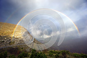 Mountain pass road with stormy clouds and rainbow