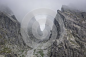 Mountain pass surrounded by fog, grey rocks in the mountains, passage between the peaks, invisible due to low clouds, in Tatra Mou