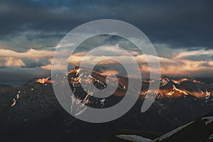 Mountain peak sunset landscape with gloomy dramatic mainly cloudy sky and orange and red sun beams