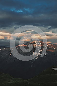 Mountain peak sunset landscape with gloomy dramatic mainly cloudy sky and orange and red sun beams