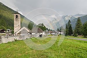 Mountain with rainbow and characteristic stone church. Traditional alpine village, Macugnaga, Piedmont, Italy